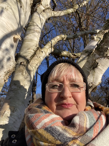 Tine mit Mütze und Schal angelehnt an einen Birkenbaum